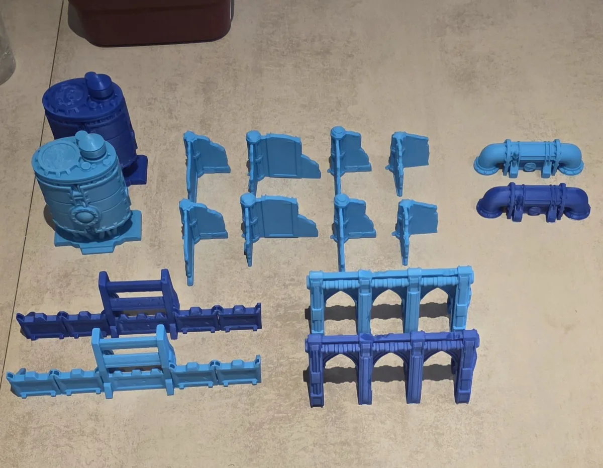 Conjunto de escenografía impresa en filamento azul: contenedores, barricadas, tuberías y una arcada en ruinas